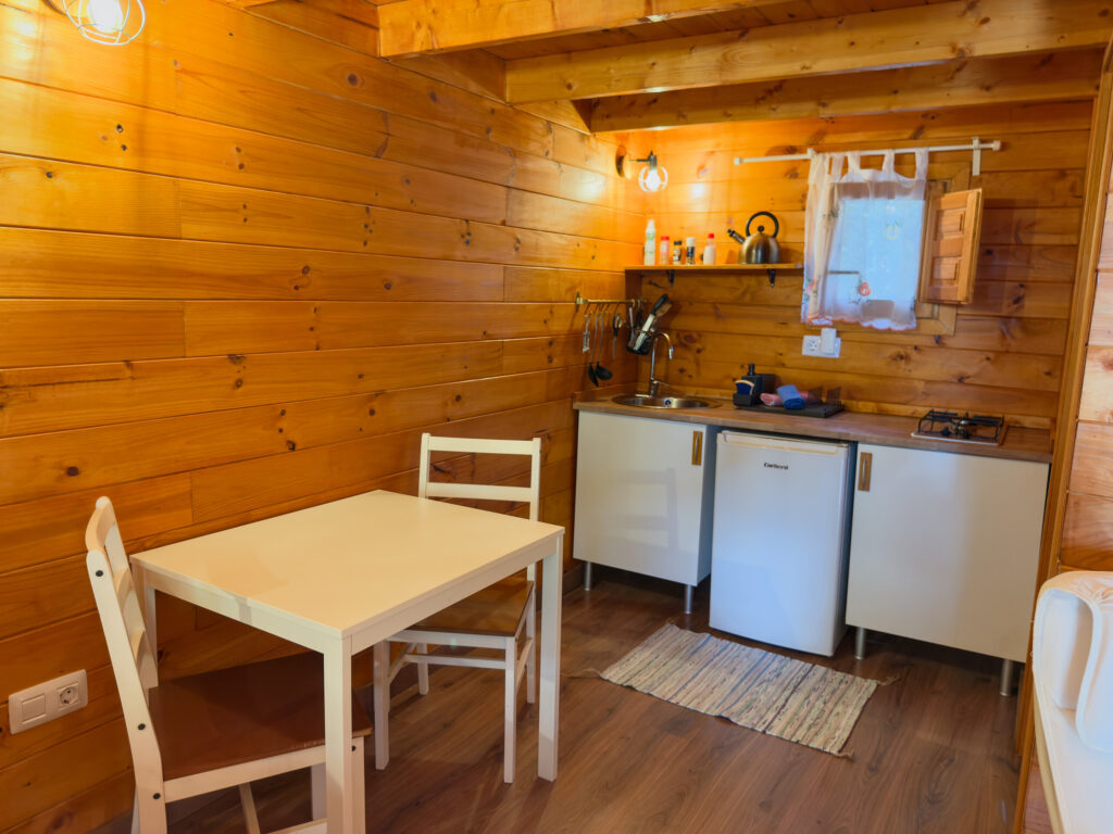 Small kitchen with hob, fridge, coffee maker and a table for two inside a wooden cabin