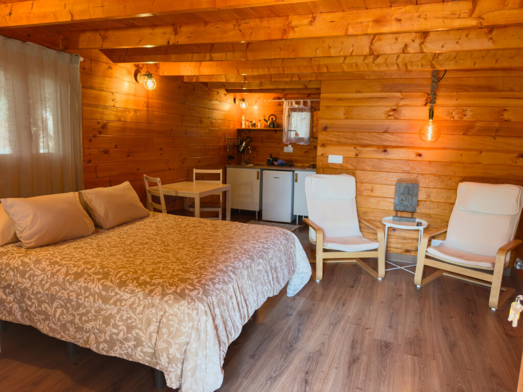 Inside a wooden cabin with a double bed, two armchairs and a kitchen in Lanzarote