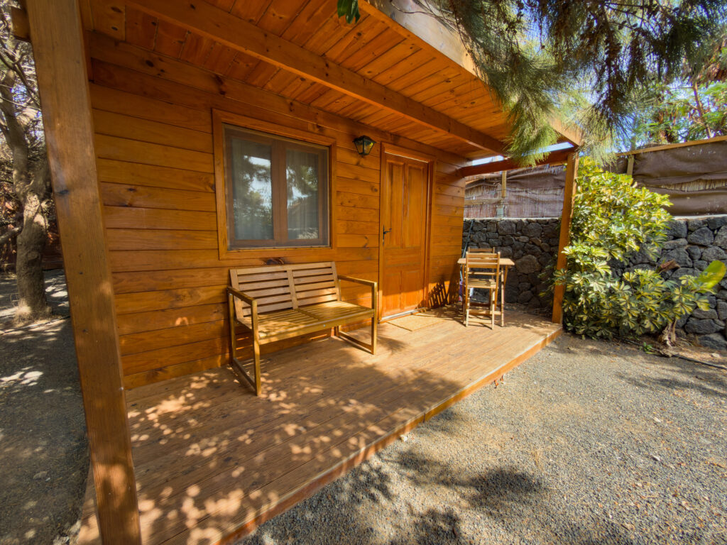 Wooden porch with a bench and table in the shade of trees, in front of a cabin in Lanzarote